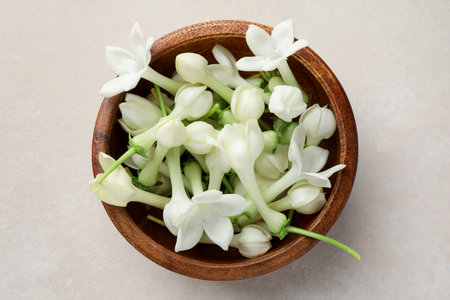 Bowl with jasmine flowers on beige table, top view