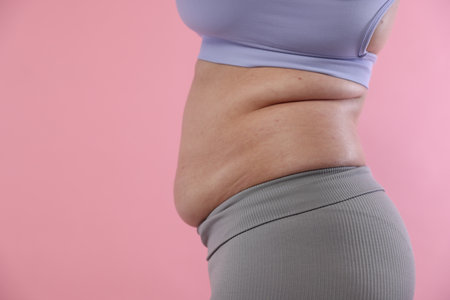 Woman with excessive belly fat on pink background, closeup and space for text. Overweight problemの写真素材