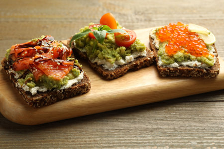 Different delicious avocado sandwiches on wooden table, closeup