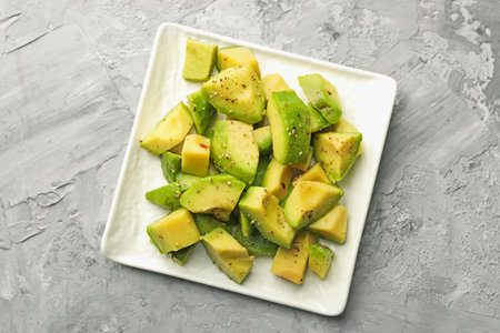 Tasty cut avocados with dressing on grey textured table, top view