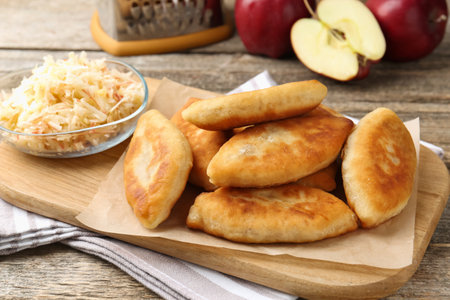 Delicious fried pyrizhky (stuffed pies) and apples on wooden table, closeupの写真素材