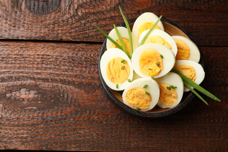 Halves of hard boiled eggs with green onions on wooden table, top view. Space for text