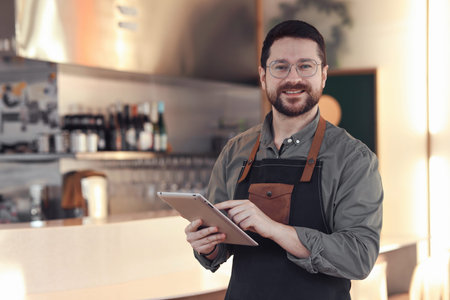 Portrait of smiling business owner with tablet in his cafe. Space for text