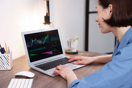 Stock exchange. Woman analyzing financial market on laptop at wooden table indoors