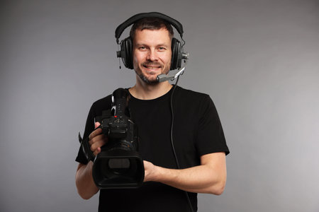 Man with professional video camera and headset on gray background
