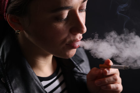 Woman smoking cigarette on black background, closeup