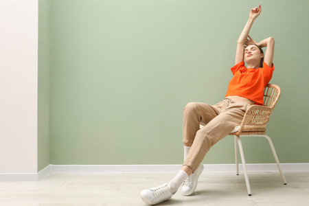 Beautiful woman relaxing in comfortable wicker armchair near pale green wall indoors, space for text