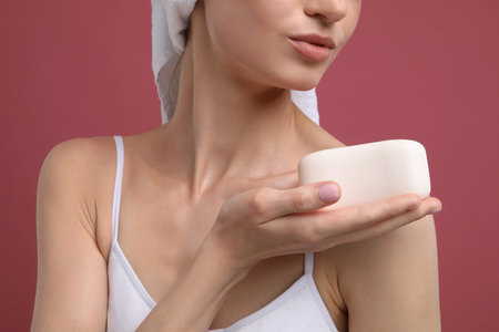 Woman with soap bar on pink background, closeup