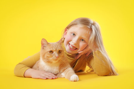 Little girl with her cute ginger cat on yellow backgroundの写真素材
