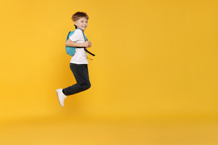 Cute schoolboy with backpack jumping on orange background, space for textの写真素材