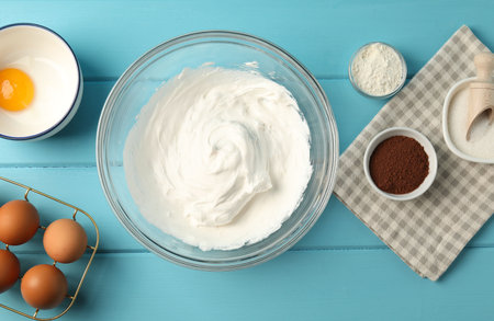 Bowl with whipped cream and ingredients on light blue wooden table, flat lay
