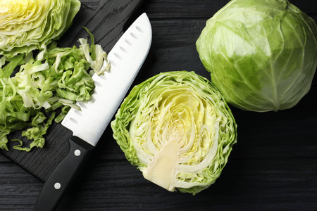 Fresh cabbages and knife on black wooden table, flat lay