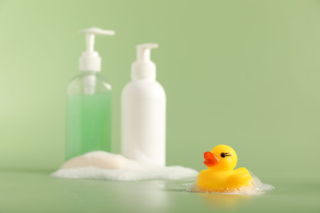 Cute rubber duck, foam, soap and bottles of cosmetic products on green backgroundの写真素材