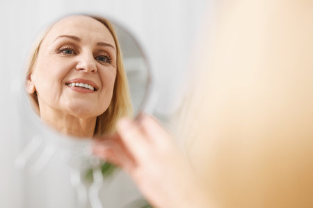 Smiling middle aged woman with round mirror on blurred backgroundの写真素材
