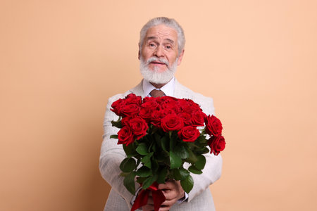 Senior man with bouquet of red roses on beige backgroundの写真素材