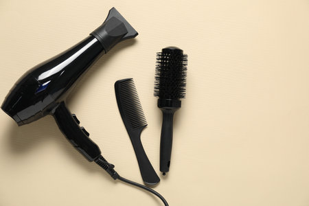 Round brush, comb and dryer on beige background, flat lay. Space for textの写真素材