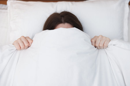 Woman covering herself with blanket on bed at home, above view. Insomnia problem