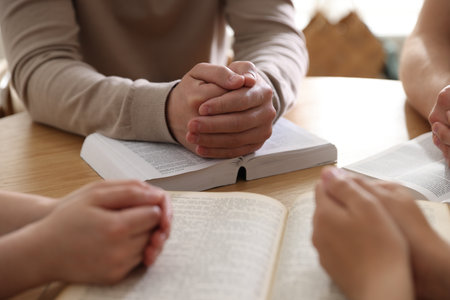 Family with Bibles praying at wooden table indoors, closeupの写真素材