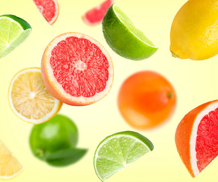 Different fresh citrus fruits in air on light yellow backgroundの写真素材