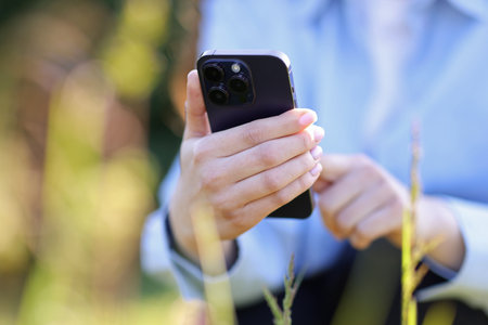 Woman using plant recognition application on smartphone outdoors on sunny day, closeupの写真素材