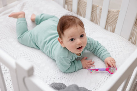 Cute little baby with rattle toy in crib at home