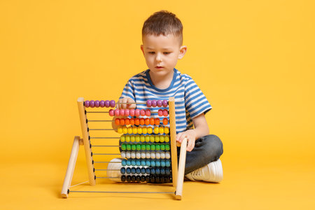 Cute little boy playing with wooden abacus on yellow backgroundの写真素材