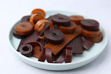 Tasty fruit leather rolls on white table, closeup