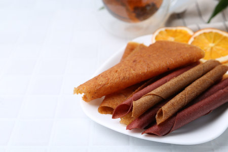 Tasty fruit leather rolls on white table, closeup. Space for text