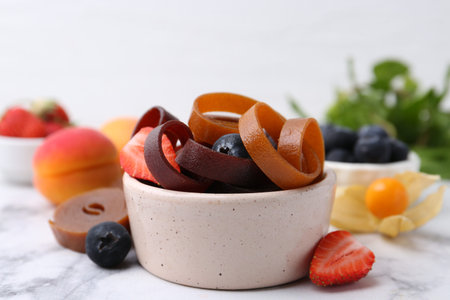 Tasty fruit leather rolls in bowl and berries on white marble table, closeupの写真素材