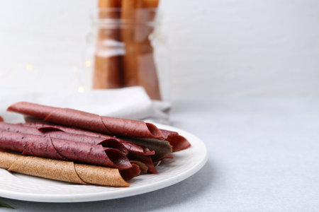 Tasty fruit leather rolls on white table, closeup. Space for text