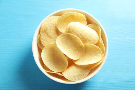 Tasty potato chips in bowl on light blue wooden table, top view