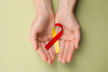 World Hepatitis Day. Woman with yellow-red awareness ribbon on olive background, top view