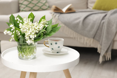 Bouquet of beautiful lily-of-the-valley and cup of tea on coffee table indoorsの写真素材