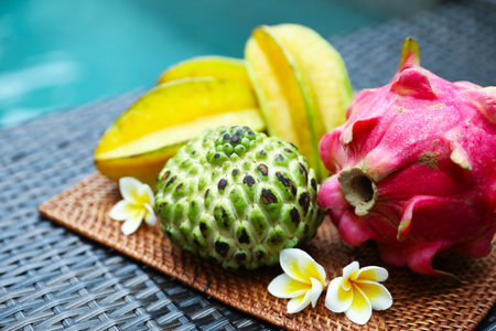 Different tropical fruit on wicker table near swimming pool, closeupの写真素材