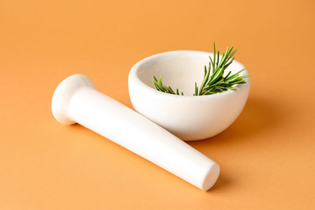 Ceramic mortar with rosemary and pestle on light brown background, closeup