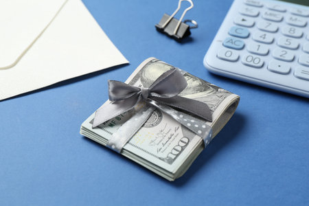 Money bonus. Dollar banknotes with bow, calculator and envelope on blue background, closeup