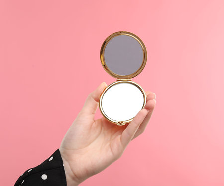 Woman holding open pocket mirror on pink background, closeupの写真素材