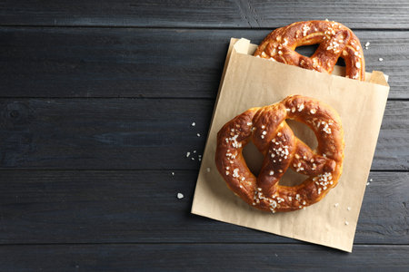 Tasty pretzels with salt on dark wooden table, top view. Space for text