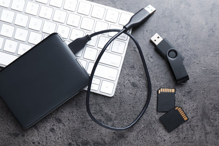 SD memory cards, USB flash drive, hard disk drive with cable and keyboard on dark grey table, flat...