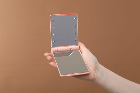 Woman holding open pocket mirror on brown background, closeupの写真素材