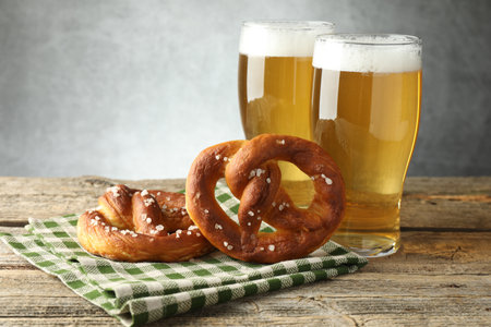 Tasty pretzels and glasses of beer on wooden table against grey background, closeupの写真素材