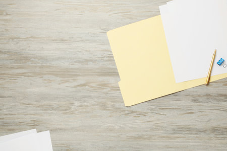 Paper file folder with blank sheets, pen and binder clip on wooden table, flat lay. Space for textの写真素材