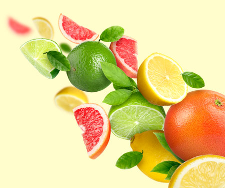 Different fresh citrus fruits and green leaves in air on beige backgroundの写真素材