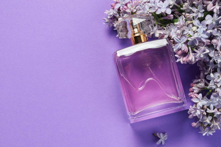 Bottle with perfume and lilac flowers on violet background, flat lay. Space for text