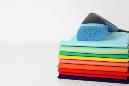 Upright steamer and stack of folded clothes on white table, closeup. Space for textの写真素材