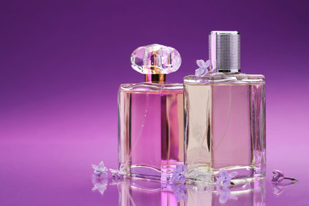Bottles with perfumes and lilac flowers on mirror surface against color gradient background,...