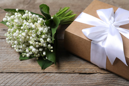 Bouquet of beautiful lily-of-the-valley flowers and gift on wooden background, closeupの写真素材