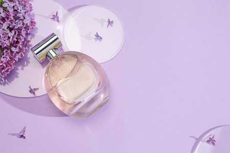 Bottle of perfume and beautiful lilac flowers on light violet background, flat lay. Space for textの写真素材