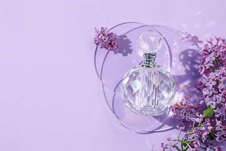 Bottle of perfume and beautiful lilac flowers on light violet background, flat lay. Space for textの写真素材