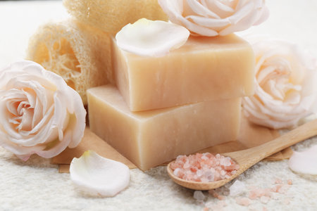 Soap bars, sea salt, loofah sponges and flowers on white textured table, closeupの写真素材